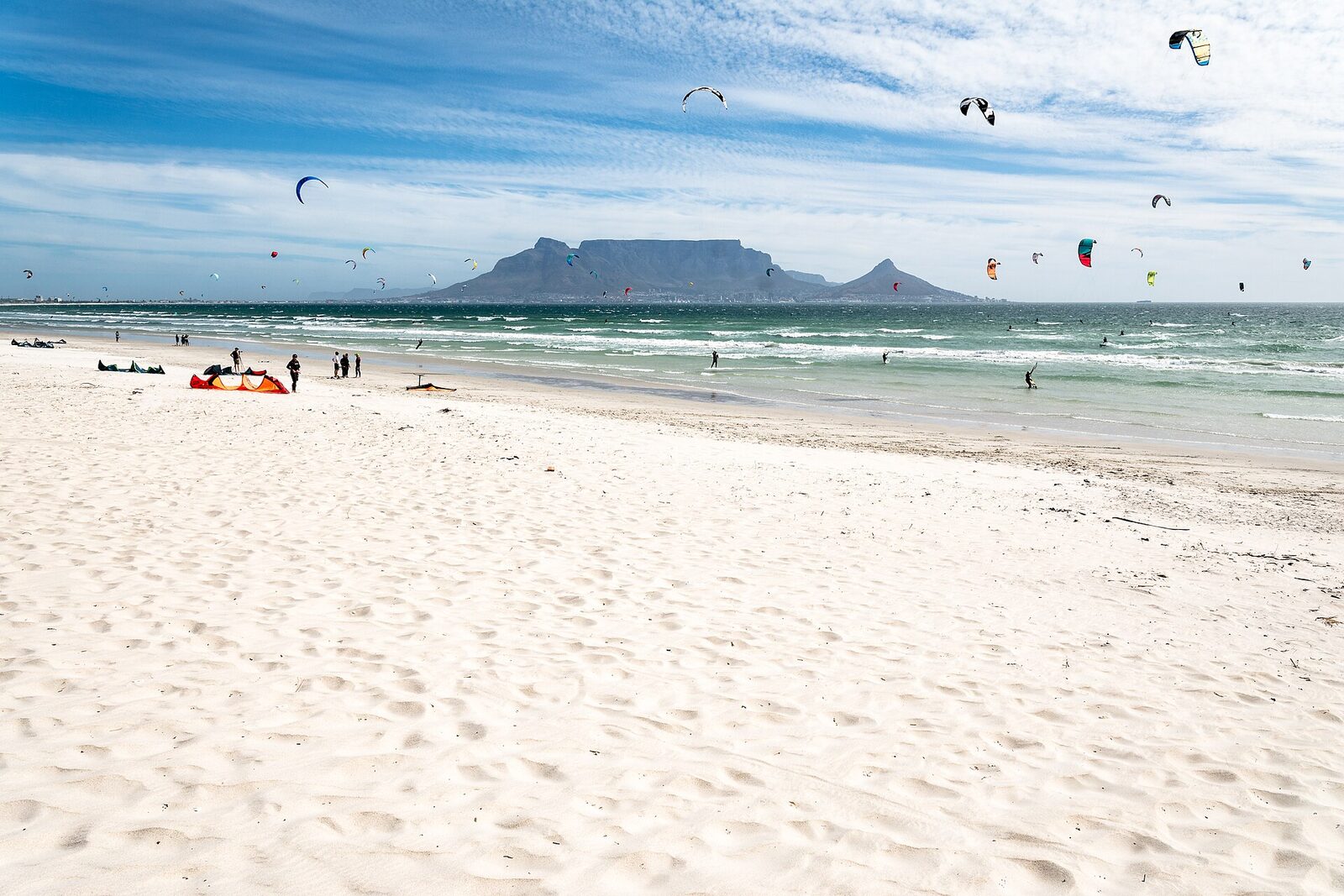 People and kitesurfers on Bloubergstrand beach with Table Mountain across the bay